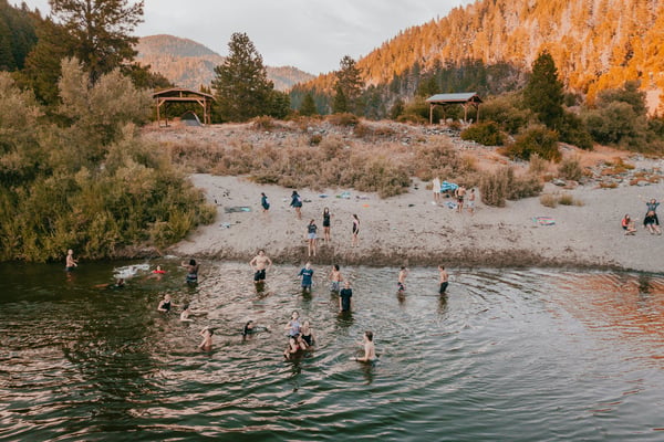 People wading and swimming in a river with golden pine-covered hills behind
